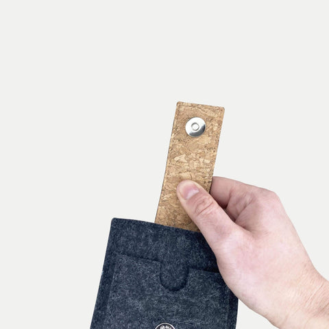 Hand, die eine graue Filzhülle für ein Smartphone mit Korkgriff und Druckknopfverschluss hält, speziell für das Motorola Moto G56 entwickelt.